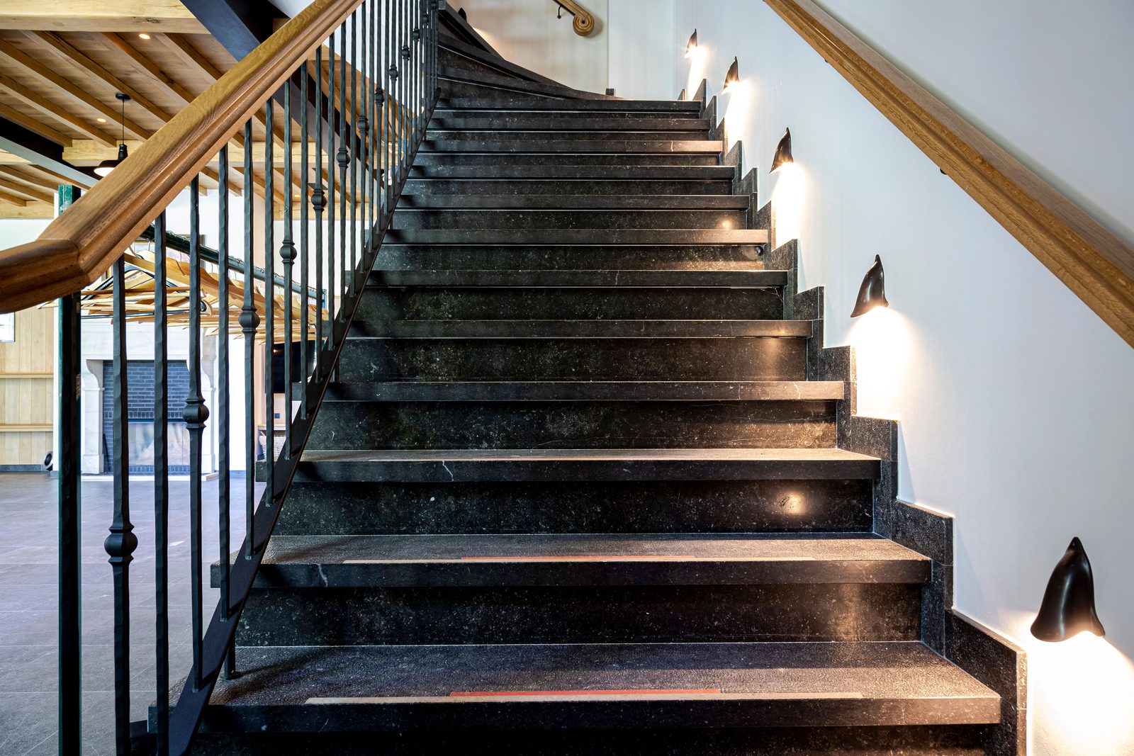 Binnentrap met donkere natuurstenen treden, smeedijzeren balusters en wandverlichting